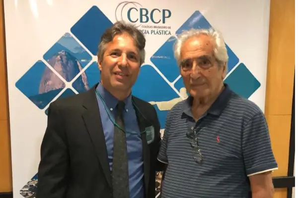 Doutor Eduardo Teixeira e seu pai doutor Edison Teixeira em frente do banner do congresso de 2019.